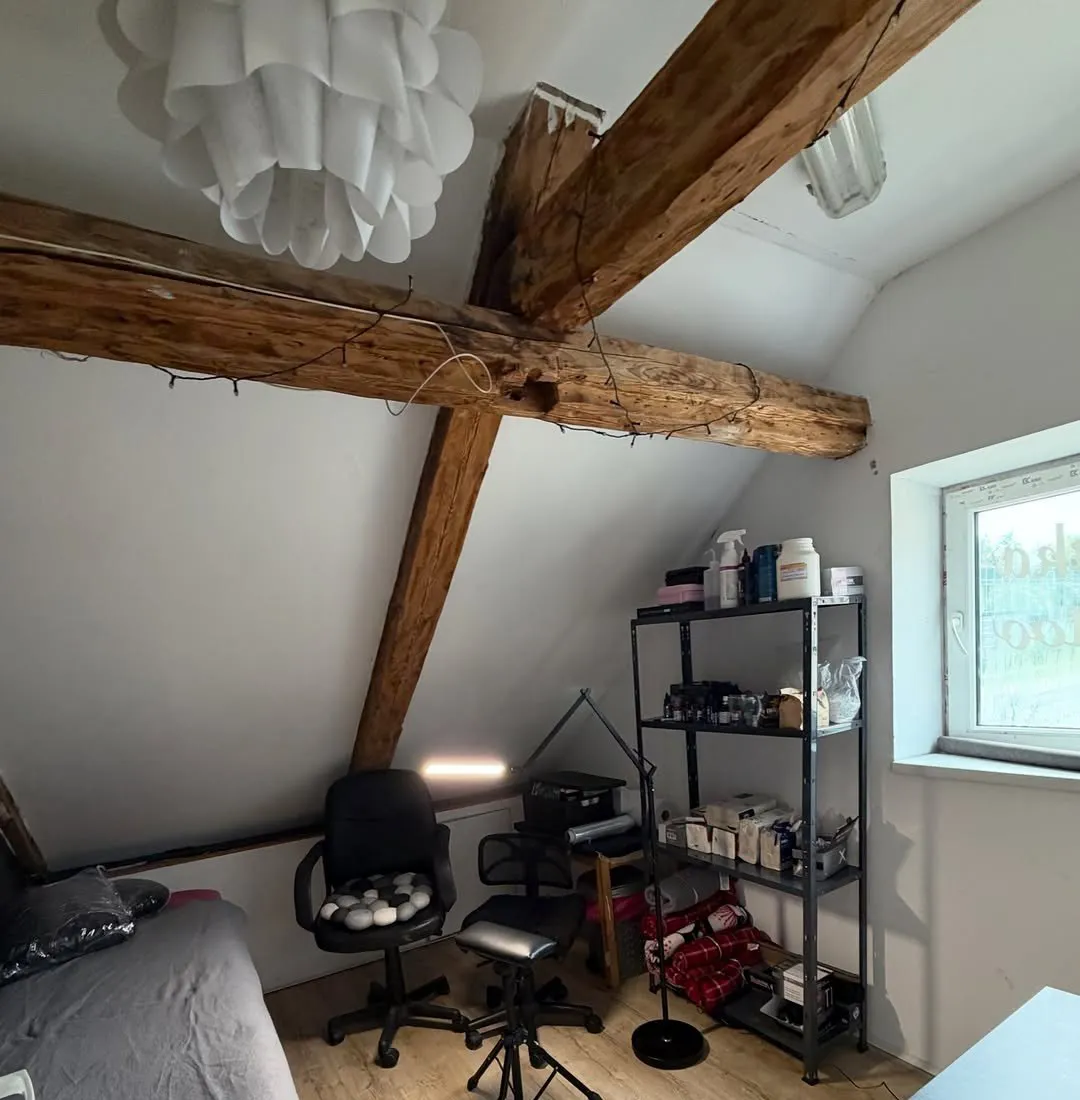 Studijas telpa bēniņos ar koka sijām, krēsliem un plauktu
